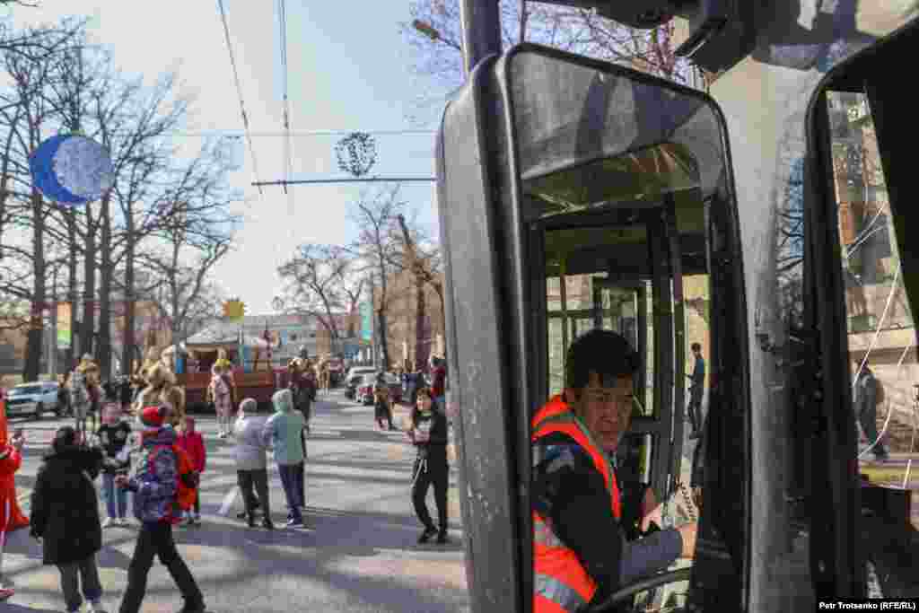 Автобус жүргізушісі терезеден шеруге көз салып отыр. 
