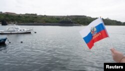 Un membru al comunității rusești din Havana flutură un steag în timp ce un submarin rusesc cu propulsie nucleară a intrat în golful capitalei cubaneze, în ultima vizită navală a Rusiei, pe 12 iunie.