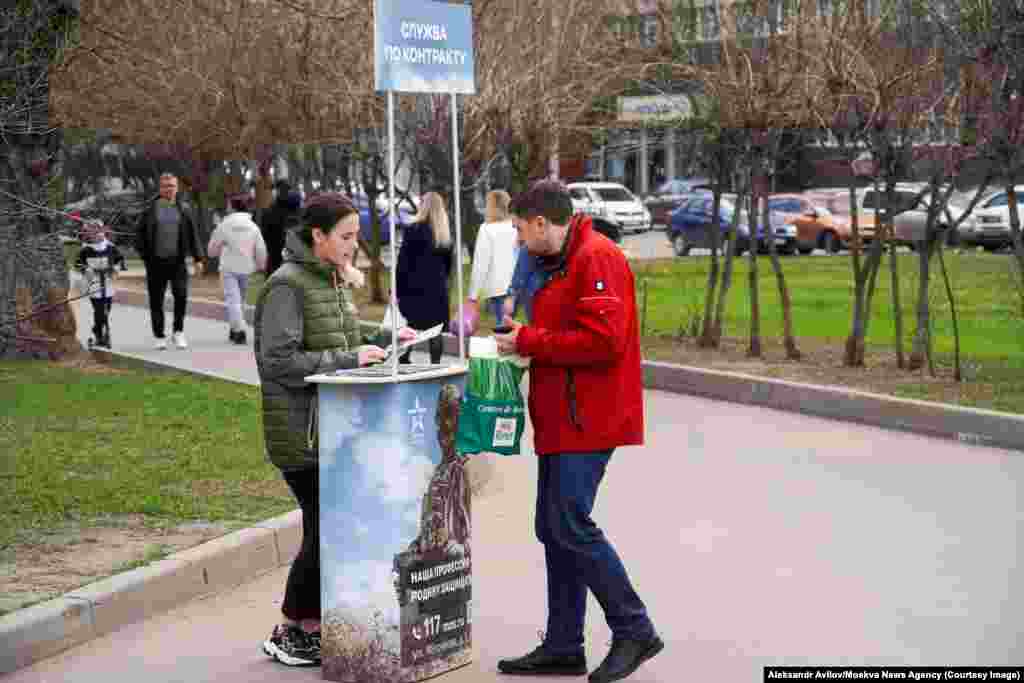 Această fotografie din 13 aprilie arată un stand din Moscova în care o tânără oferă contracte celor care doresc să ia parte la invazia rusă în Ucraina.