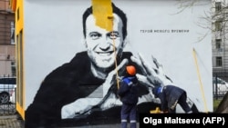 Bir işçi Nawalnynyň uly suratynyň ýüzüni reňkleýär. 