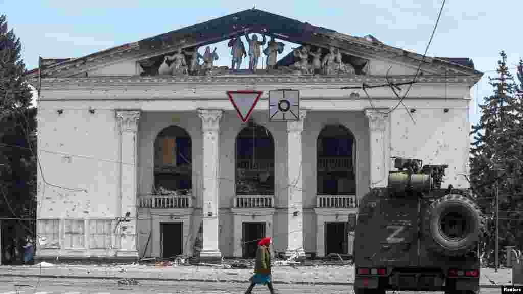 An elderly woman walks past the destroyed theater and an armored vehicle of pro-Russian forces in April 2022. 