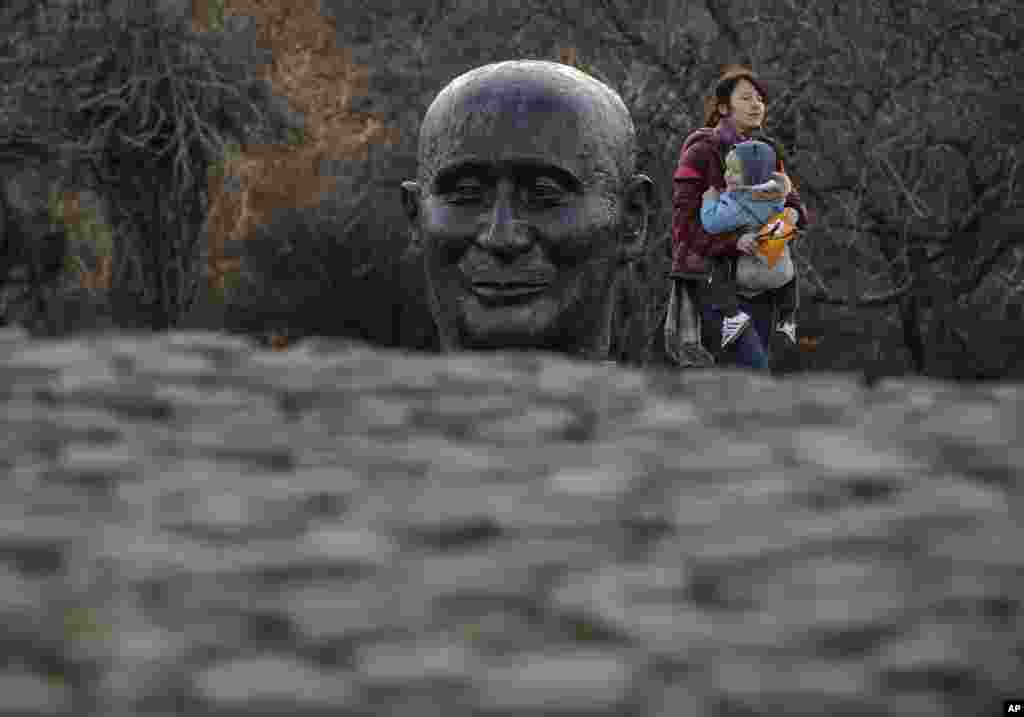 O femeie merge ținând un bebeluș pe lângă o sculptură care îl înfățișează pe diplomatul francez Jean Monnet, parte a monumentului Părinților Fondatori ai Uniunii Europene din București, România, pe 29 decembrie 2018. Uniunea Europeană a marcat joi, 9 mai, Ziua Europei, dar toată lumea privește spre alegerile care vor avea loc exact peste o lună și care prevestesc ascensiunea extremei drepte și o posibilă îndepărtare de politicile sale globale în materie de schimbări climatice.