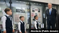 Касым-Жомарт Токаев c учениками школы имени Кемеля Токаева в городе Уштобе. На заднем плане за стеклом — фотографии писателя, отца президента. Жетысуская область, 27 октября 2023 года
