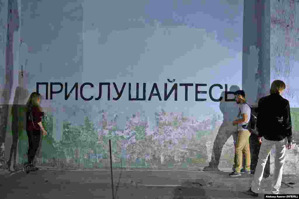 Көрме каталогында Мира Евгеньевна деп аталған қыз қабырғадағы «Құлақ салыңыз» («Прислушайтесь») деген жазудан, дыбыс күшейткіштер мен аудиодан тұратын инсталляция жасаған. Егер дыбыс күшейткішке құлағыңызды тоссаңыз бір жағынан осы заманғы жаңалықтарды, ал екінші жағынан – «Алаш» партиясы, «Алашорда» қайраткерлерінің сөздерін естуге болады. Бұл инсталляция «қазіргі заманғы адамның тоқырауы» жайлы, білімнен жұрдай адам туралы ойдың жемісі.